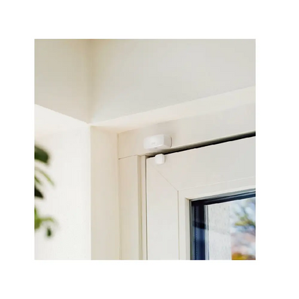 Compact white Eve smart contact sensor positioned on a window frame, showing the tool-free wireless magnetic sensor setup used to monitor open or closed status.